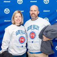 Man and woman with crewnecks on standing in front of GV backdrop